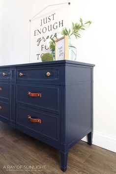 a blue dresser with gold handles and brass knobs on the top, against a white wall