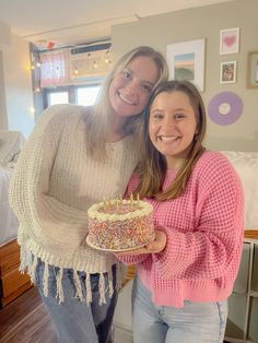 two women standing next to each other holding a cake with sprinkles on it