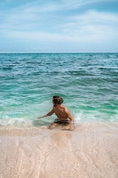 a young boy sitting in the water on top of a sandy beach next to the ocean