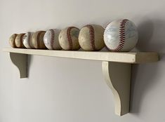 baseballs are lined up on a shelf in a room with gray walls and white paint