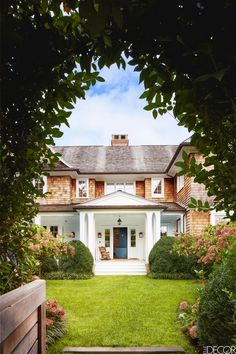 a large white house surrounded by lush green grass and bushes with pink flowers in the front yard