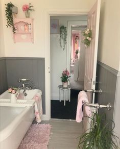 a white bath tub sitting inside of a bathroom next to a sink and window with potted plants