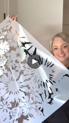 a woman holding up a large white paper cutout with flowers on it's side