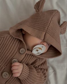 a baby is wearing a brown sweater and pacifier