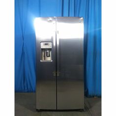 a silver refrigerator freezer sitting in front of a blue curtain with water dispenser