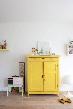 a yellow cabinet in a white room next to a lamp and pictures on the wall