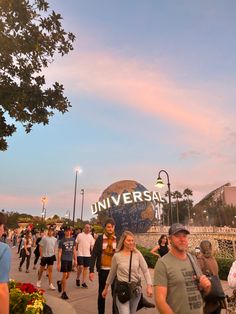 many people are walking down the sidewalk in front of an universal studios sign at sunset