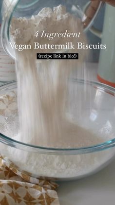 a person pouring ingredients into a bowl on top of a white countertop with the words vegan buttermik biscuits