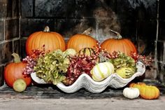 pumpkins and gourds are arranged in a bowl on a fireplace mantel