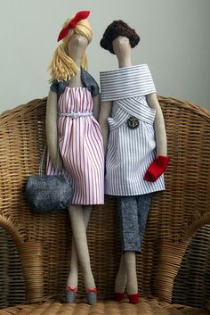 two dolls sitting on top of a wicker chair with one holding a purse and the other standing up