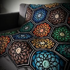 a crocheted afghan is sitting on a couch with a dark background and white walls