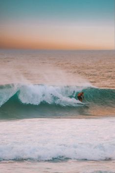 a man riding a wave on top of a surfboard in the ocean at sunset