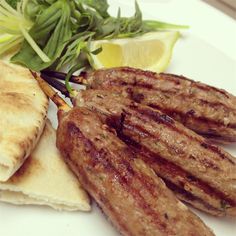 some meat and pita bread on a white plate with a lemon wedge next to it