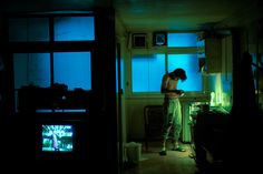 a man standing in a dark room next to a window with blue light on it