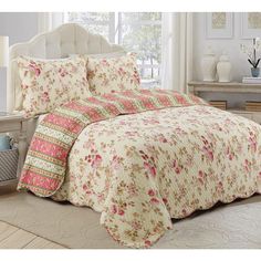 a bed with floral comforter and pillows on top of it in front of a window