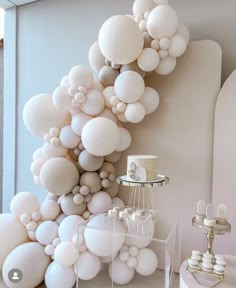 a room filled with lots of white balloons and cake on top of a table in front of a wall