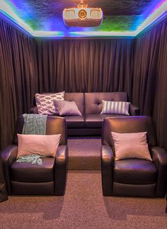 two brown leather couches sitting in front of a purple curtained area with colorful lights on the ceiling