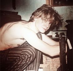 a shirtless young man leaning on a counter top with his arm wrapped around an object