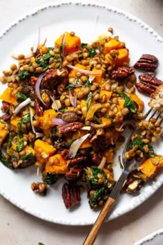 a white plate topped with vegetables and nuts next to a fork on top of a table