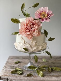 a white cake with pink flowers on top and green leaves around the edges, sitting on a wooden table