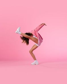 a woman in pink jacket and white sneakers doing a handstand