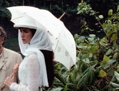 a man and woman standing next to each other with an umbrella over their heads in the rain