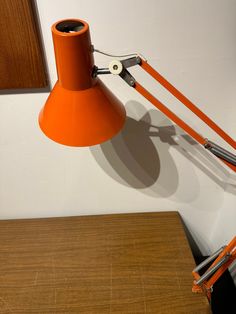 an orange desk lamp sitting on top of a wooden table next to a white wall