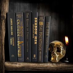 a gold skull sitting on top of a book shelf next to some books and a candle