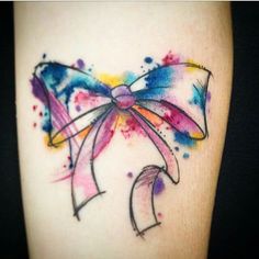 a colorful bow tattoo on the right side of the leg, with watercolor splashs all over it