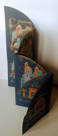 two folded greeting cards with an image of a town on them, one is blue and the other is gold