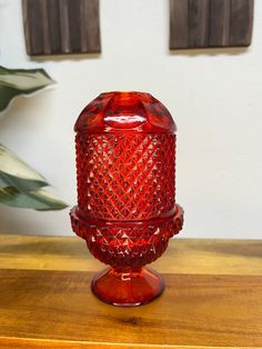 a red glass vase sitting on top of a wooden table