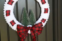 a red and white wreath with a pine tree on it hanging from the front door