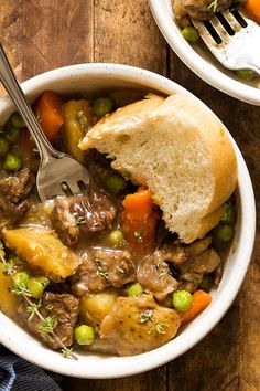 a bowl filled with meat and vegetables next to a piece of bread on top of a wooden table