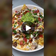 a white bowl filled with taco salad on top of a table next to a plate of tortilla chips