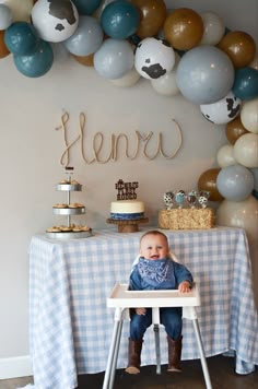 a baby sitting in a high chair next to a table with balloons and cake on it