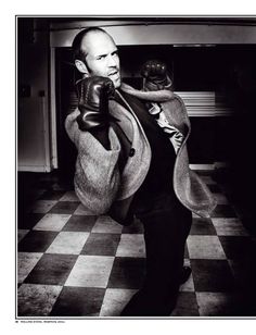 black and white photograph of a man with boxing gloves on his head, wearing a coat