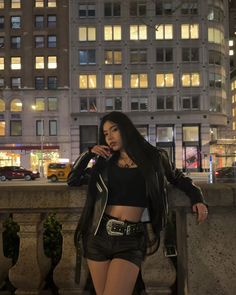 a woman in short shorts and leather jacket talking on her cell phone outside at night