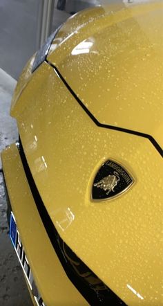 the front end of a yellow sports car with water droplets on it's hood