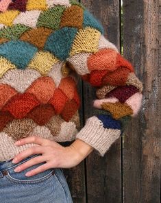 a woman standing next to a wooden fence wearing a multicolored sweater and jeans