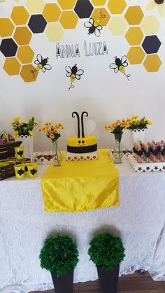 a table topped with a cake covered in yellow and black frosting next to potted plants