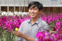 a man standing in a field full of purple flowers holding a small yellow object with one hand