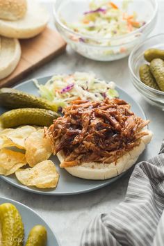 a pulled pork sandwich with pickles, coleslaw and pickles on the side