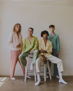 four people sitting on stools in front of a white brick wall and one person standing