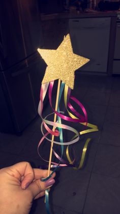 a hand holding a star shaped stick with streamers on it's end and a ribbon in the middle