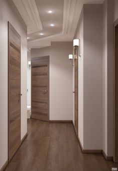 an empty hallway with two wooden doors and lights on either side of the door, leading to another room