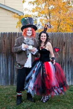 two people dressed up in costumes standing next to each other near a fence and tree