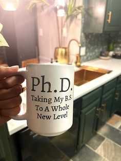 a person holding up a coffee mug in a kitchen that says, ph d taking my b's to a whole new level