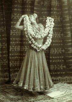 an old photo of a woman in a dress with flowers around her neck and arms