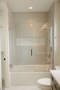 a white toilet sitting next to a bath tub in a bathroom under a light fixture