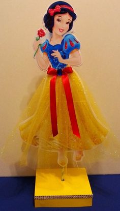 the snow queen is wearing a yellow dress with red ribbon around her waist and holding a flower